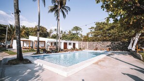 A swimming pool with lounge chairs, a stone wall, and palm trees. - Beachfront Point Break Villa @SurfCity (Conchalio)