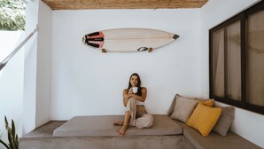A person sitting on a cushioned bench with a surfboard mounted on the wall above. - Beachfront Beach Break Villa @SurfCity (Conchalio)