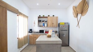 A modern kitchen with wooden cabinets, a central island, a refrigerator, and decorative wall art. - Beachfront Beach Break Villa @SurfCity (Conchalio)