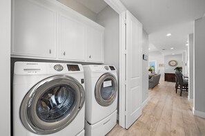 A laundry room with two Samsung washing machines, a white cabinet, and a dining area with a table and chairs. - Sandcastle by Ryson Vacation Rentals (Galveston)