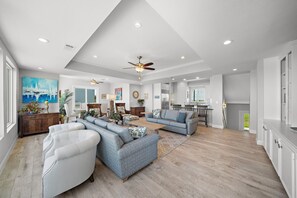 A spacious living room with a sectional sofa, a coffee table, and a ceiling fan. - Sandcastle by Ryson Vacation Rentals (Galveston)