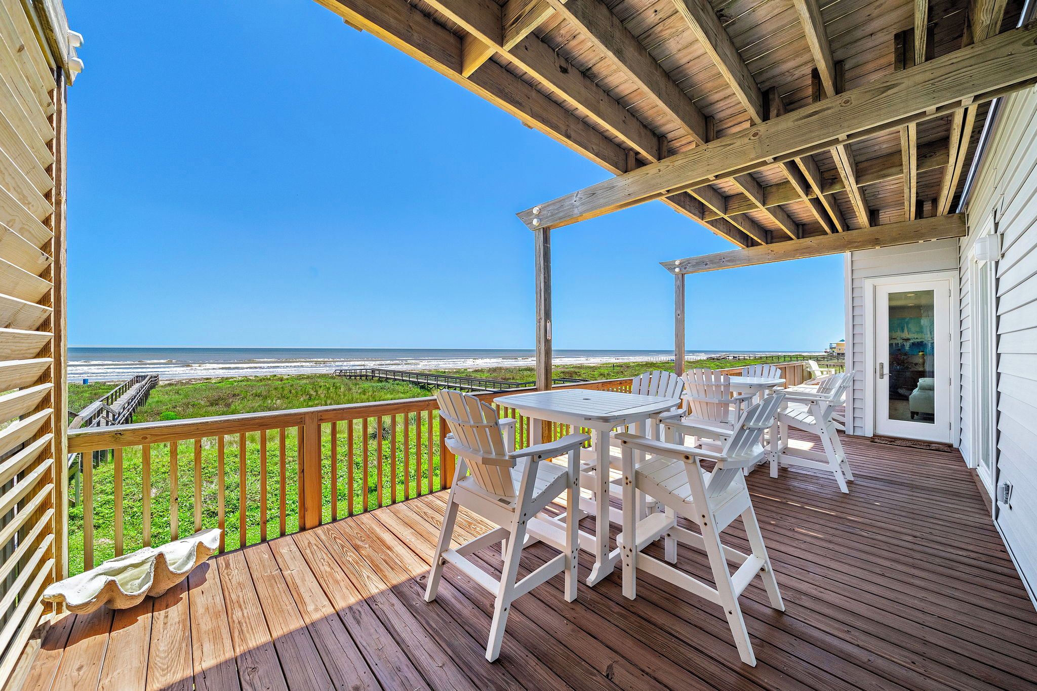 Eine Holzterrasse mit Tisch und Stühlen mit Blick auf einen Strand.