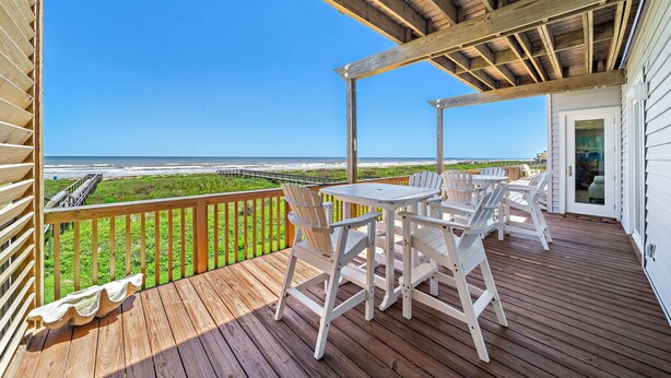 A wooden deck with a table and chairs overlooking a beach. - Sandcastle by Ryson Vacation Rentals (Galveston)