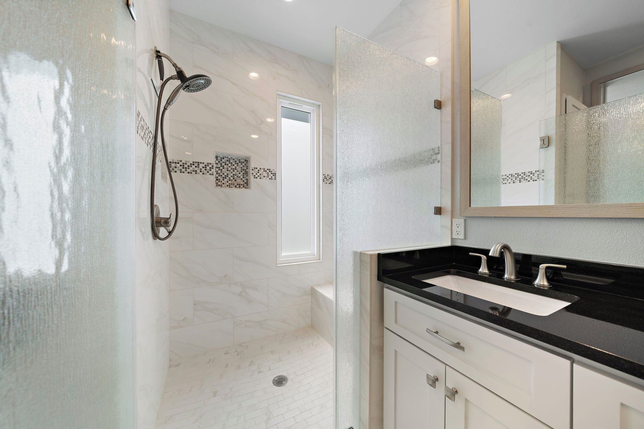 Un baño moderno con ducha de vidrio, lavamanos de superficie negra y muebles de color blanco.