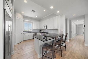 A modern kitchen with white cabinets, a central island, and a dining area with chairs. - Sandcastle by Ryson Vacation Rentals (Galveston)