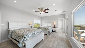 A bedroom with two beds, a ceiling fan, and a view of the ocean. - Sandcastle by Ryson Vacation Rentals (Galveston)