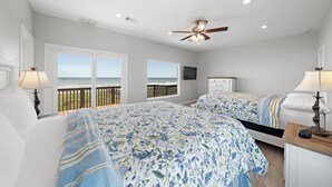 A bedroom with two beds, a ceiling fan, and a balcony with a view. - Sandcastle by Ryson Vacation Rentals (Galveston)