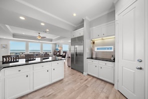 A spacious kitchen with white cabinetry, a large island, and a view of the ocean. - Sandcastle by Ryson Vacation Rentals (Galveston)