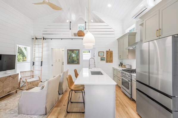 A modern kitchen with white cabinetry, a central island, stainless steel appliances, and a dining area with wicker chairs.