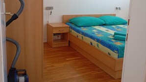 A small, neatly arranged bedroom with a wooden bed, a nightstand, and a vacuum cleaner.