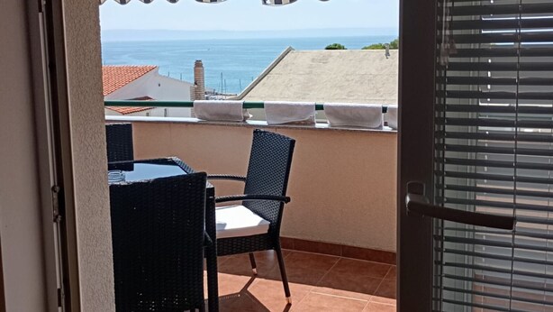 A balcony with a view of the sea, a table, and two chairs.