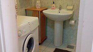 A small bathroom with a washing machine, a sink, and toiletries on a shelf.