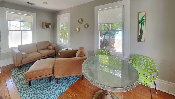Uma sala de estar com um sofá bege, uma mesa de jantar com tampo de vidro e uma poltrona verde.