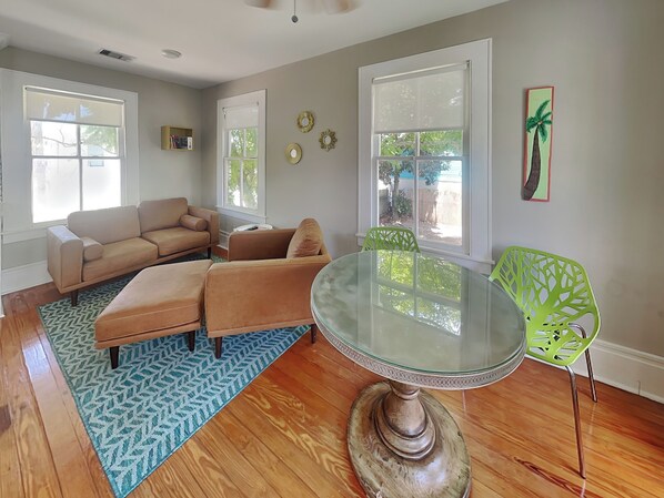 A living room with a beige sofa, a glass-top dining table, and a green chair.
