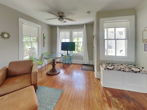 A living room with a brown leather sofa, a round glass coffee table, a teal side table, and a white bench with a patterned cushion.