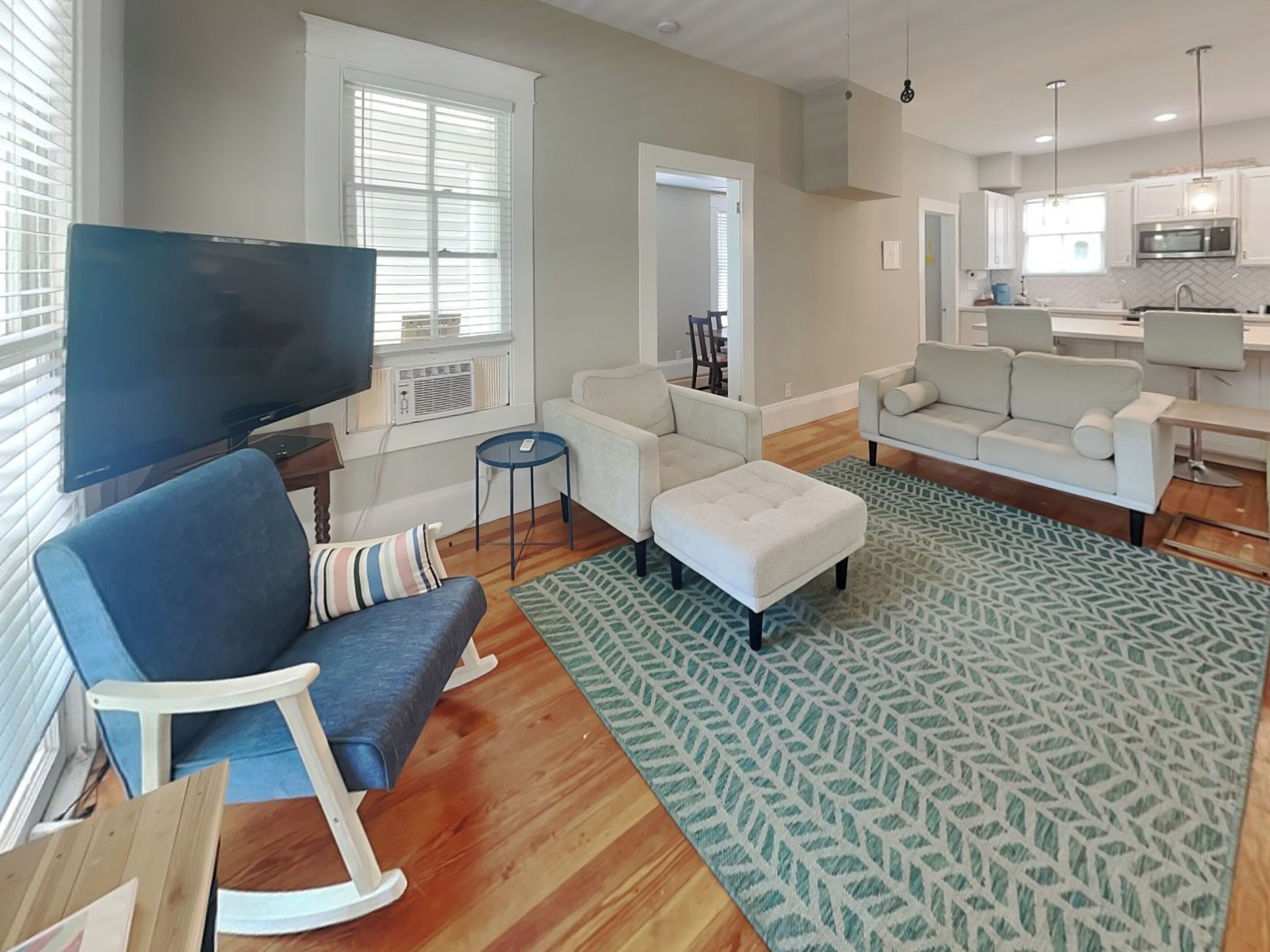 A modern living room with a flat-screen TV, a blue sofa, a white armchair, and a patterned rug.