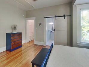 A bedroom with a bed, a dresser, a fan, a door, and a window.