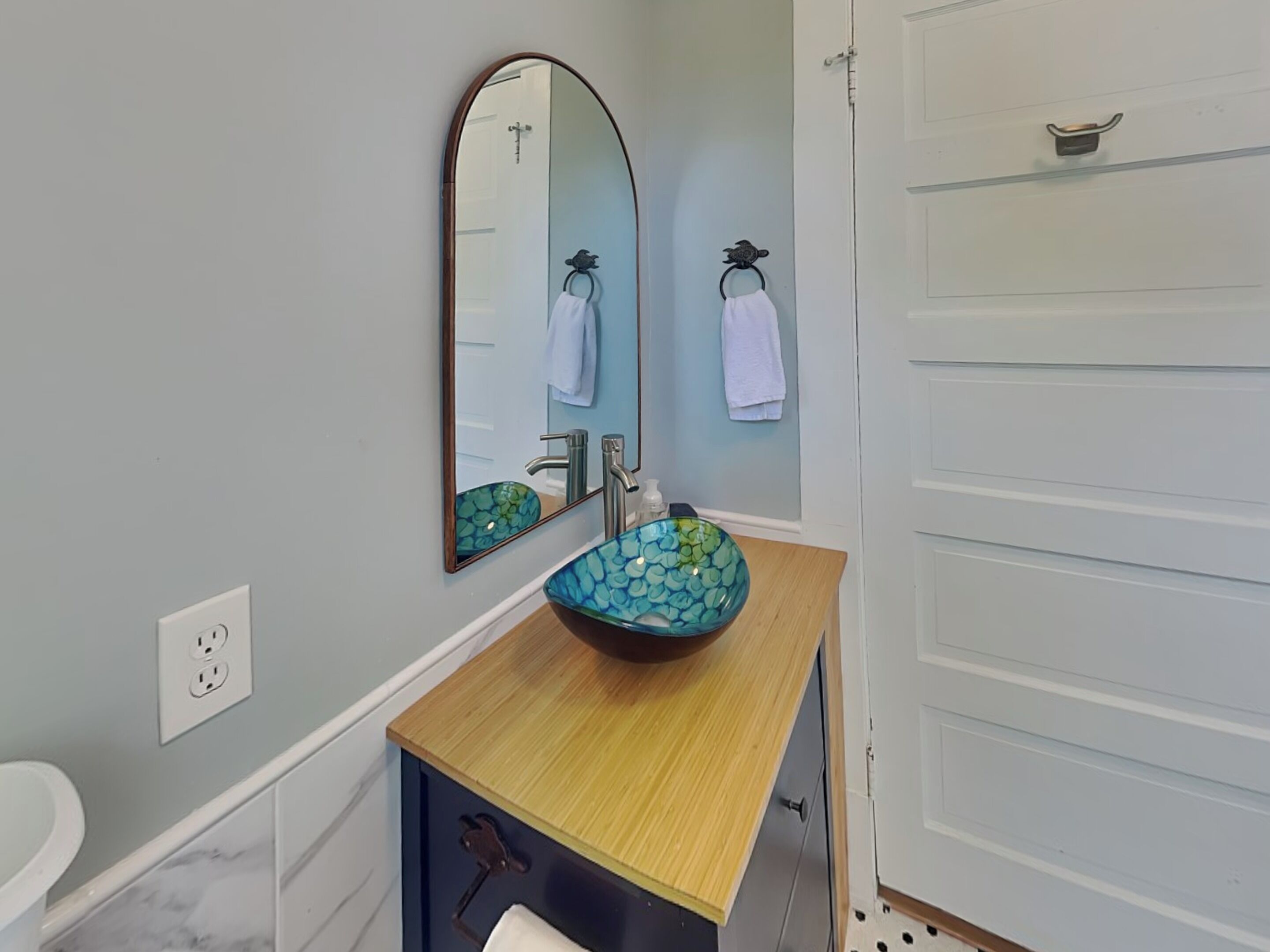 A bathroom with a wooden vanity, a glass bowl sink, a mirror, and a towel rack.