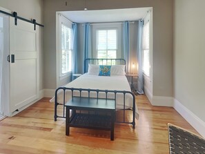 A bedroom with a bed, a bedside table, a window with curtains, and a door.
