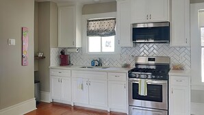 Cozinha moderna com armários brancos, fogão de aço inoxidável e micro-ondas.