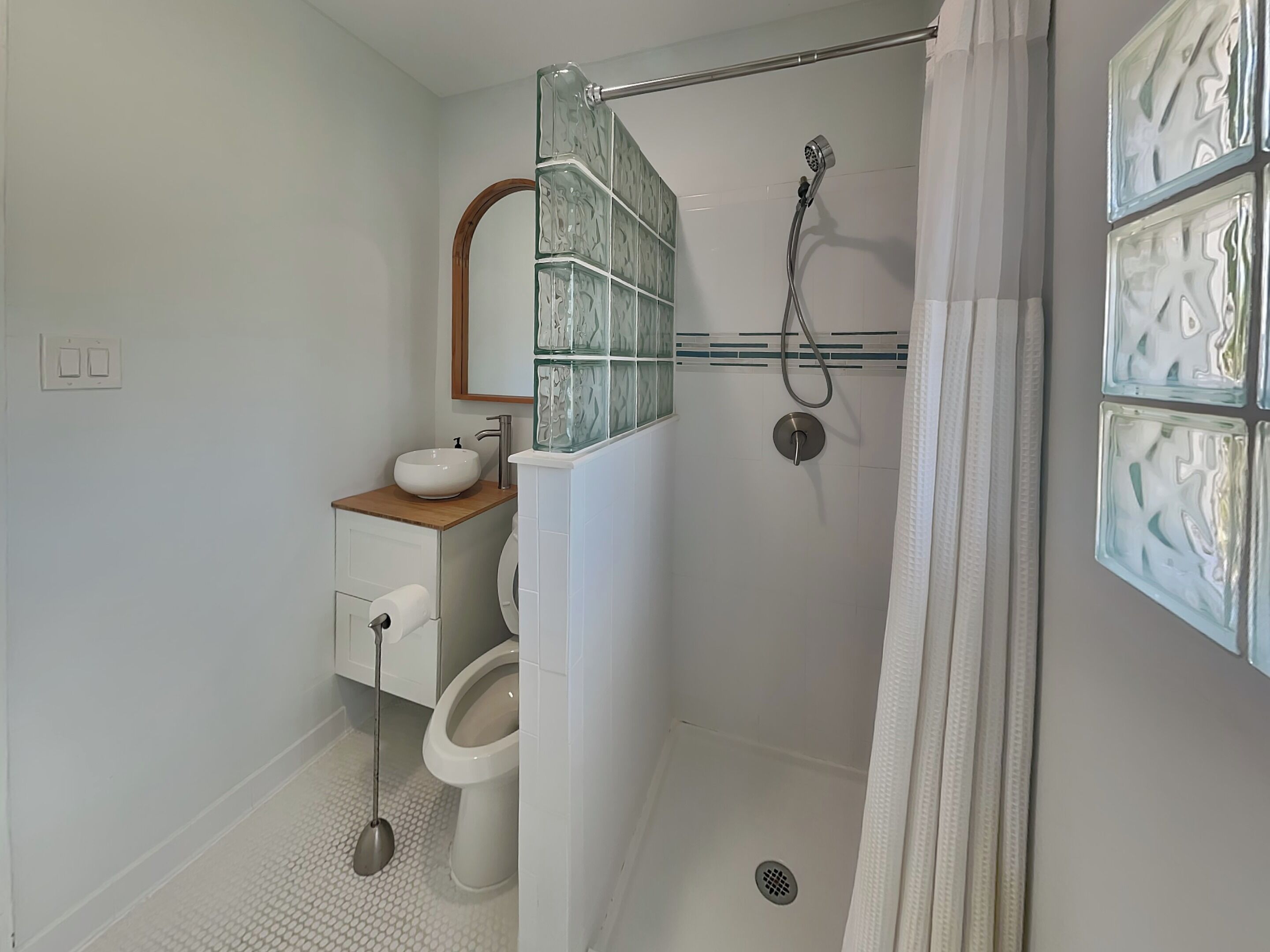 Een badkamer met een douchecabine van glas, een toilet, een wastafel met houten blad en een spiegel.