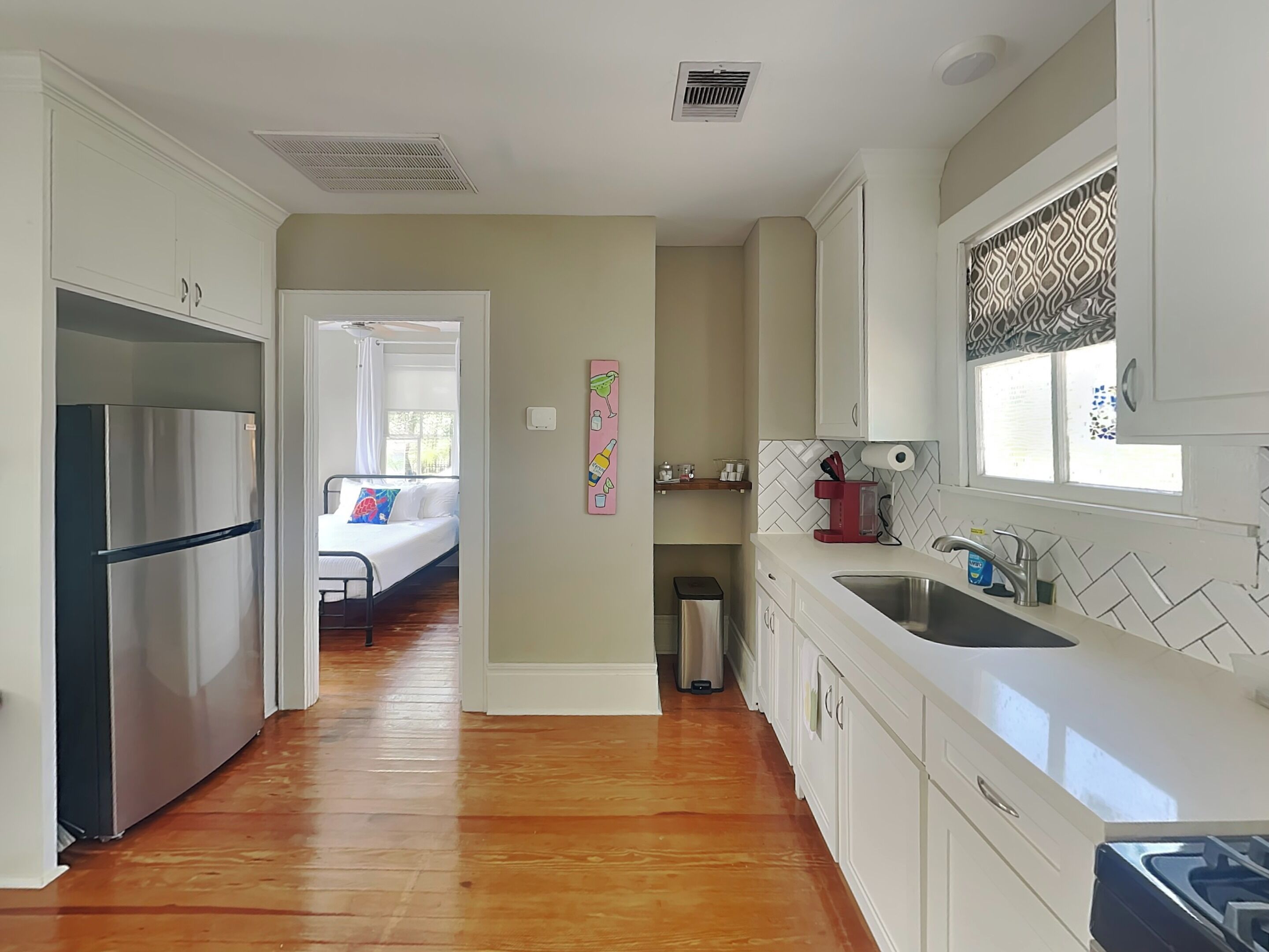 A modern kitchen with white cabinets, a stainless steel refrigerator, a sink, and a window with patterned curtains.