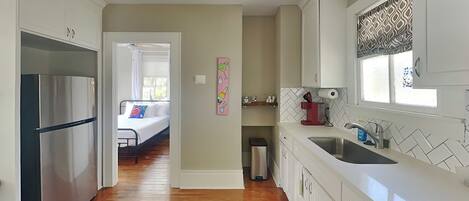 A modern kitchen with white cabinets, a stainless steel refrigerator, a sink, and a window with patterned curtains.