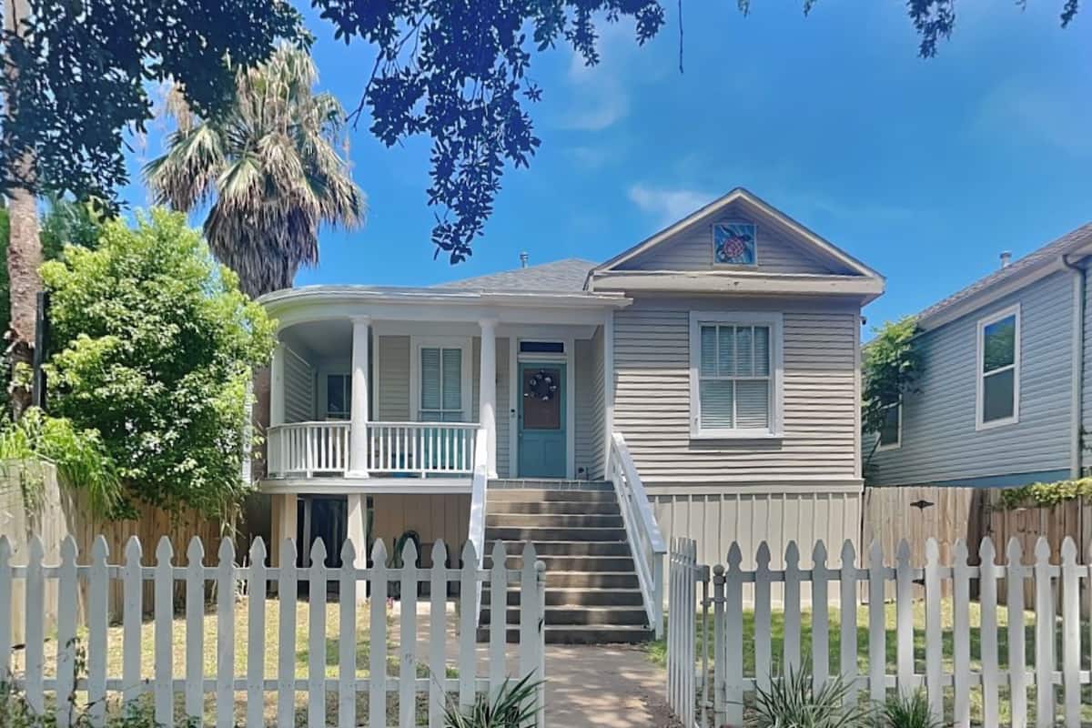 A two-story house with a front porch, a small front yard, and a picket fence.