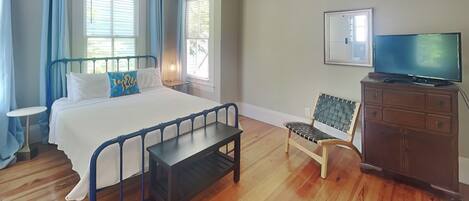 A bedroom with a bed, a bench, a chair, a TV, and a dresser.