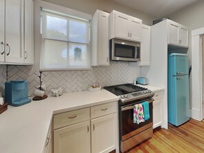 A modern kitchen with white cabinets, a stainless steel stove, a blue refrigerator, and a window with a view of the outdoors.