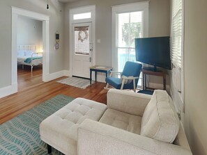 A living room with a sofa, a television, and a chair. There is a door with a window and a small table.