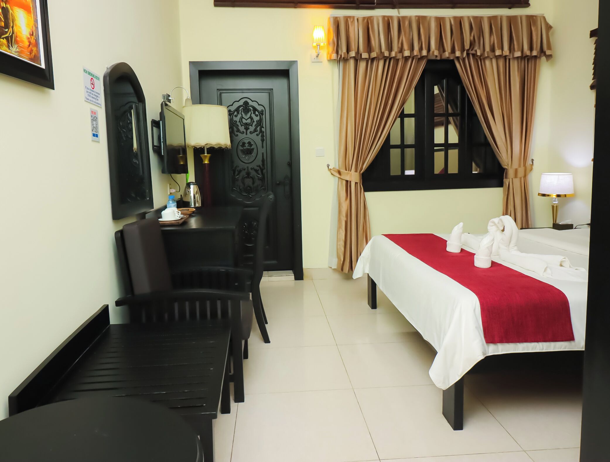 A hotel room with a bed, a desk, a chair, a door, and a window with curtains.