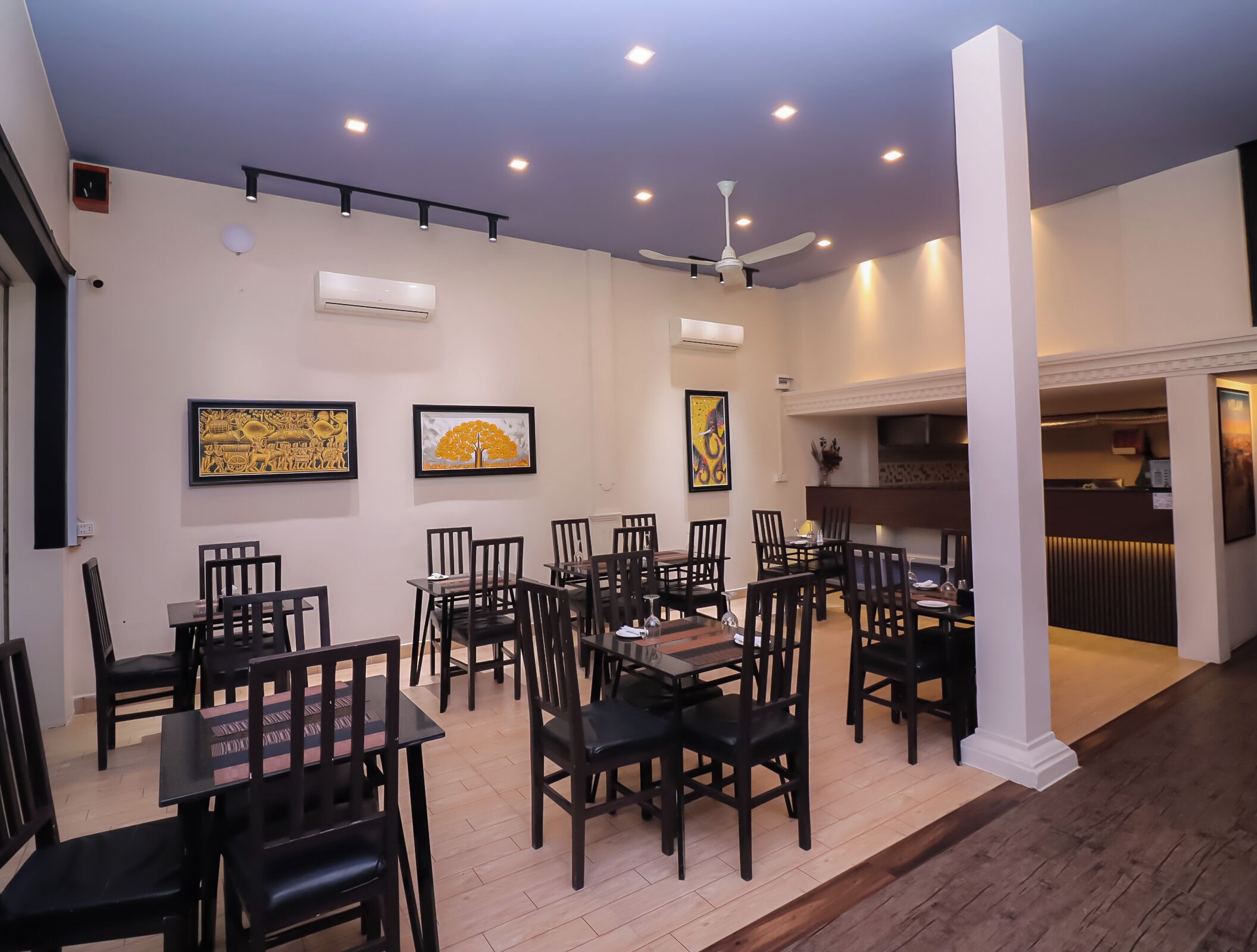 A dining area with multiple tables and chairs, ceiling fans, recessed lighting, and wall-mounted artwork.