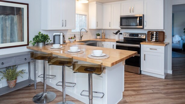 A modern kitchen with white cabinets, a wooden island with bar stools, stainless steel appliances, and a framed picture on the wall. - Shanah's Vacation Rentals (Grayland)