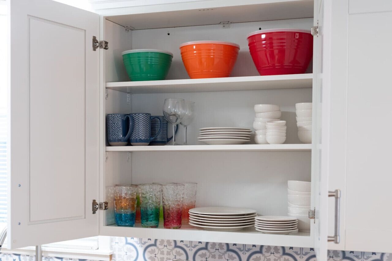 A kitchen cabinet with colorful bowls, plates, and glasses.