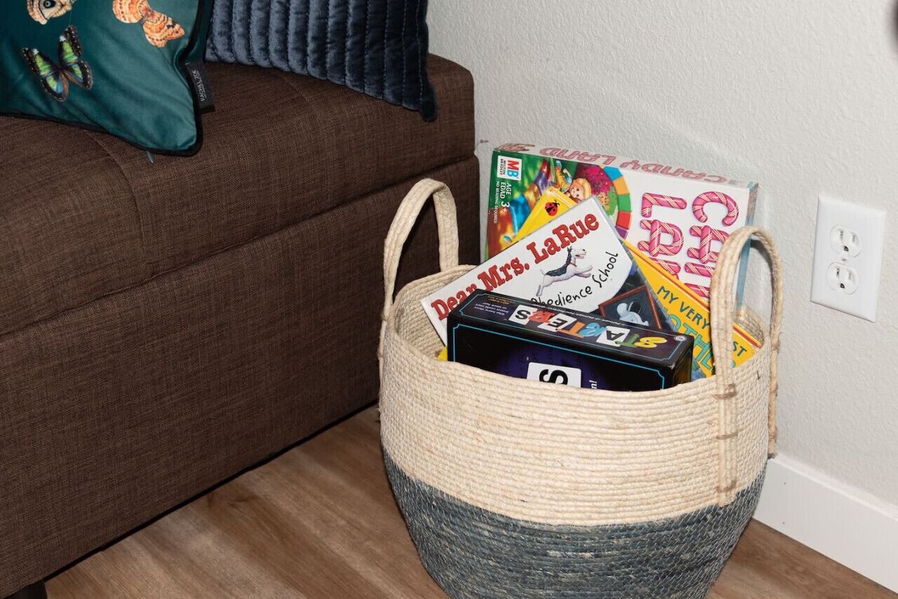 Una cesta tejida llena de libros infantiles sobre un sofá marrón.