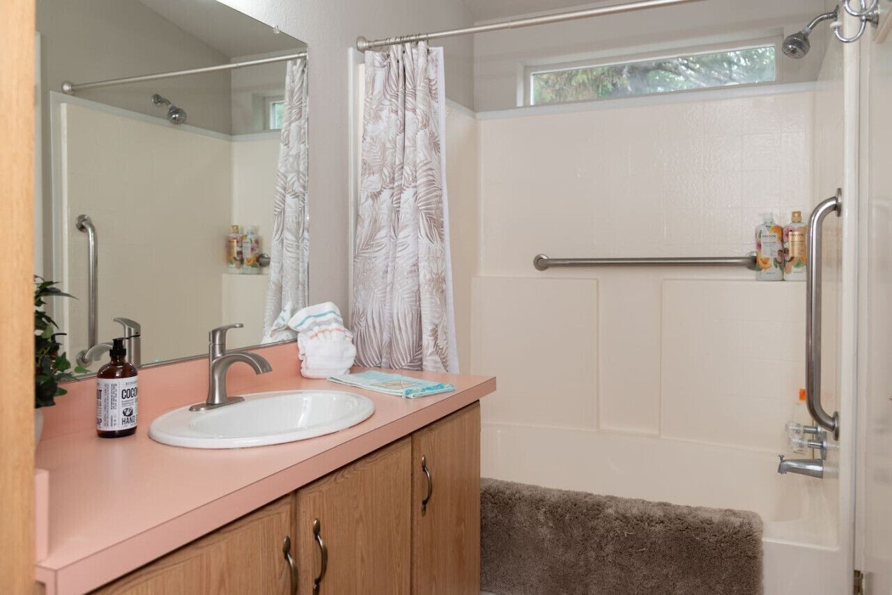 A bathroom with a pink vanity, a white sink, a mirror, and a shower with a white door.