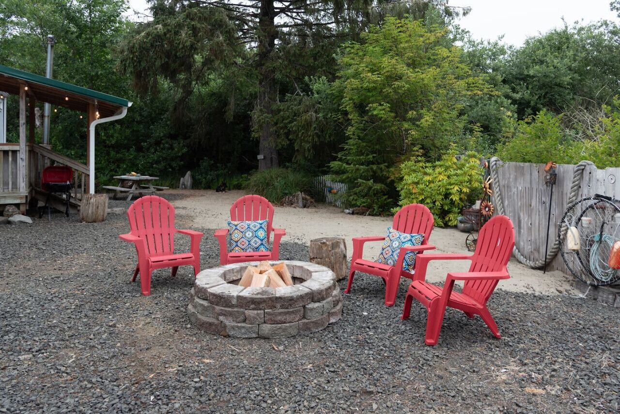 A fire pit with red Adirondack chairs and a wooden deck.