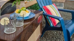 A wooden table with a plate of food, glasses, and a chair with a colorful cushion. - Shanah's Vacation Rentals (Grayland)