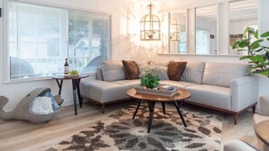 A living room with a sofa, a coffee table, a small side table, and a large window with blinds. - Shanah's Vacation Rentals (Grayland)