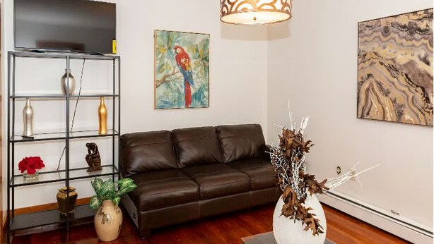A living room with a dark brown leather sofa, a glass shelving unit with decorative items, a large abstract painting, and a modern pendant light.