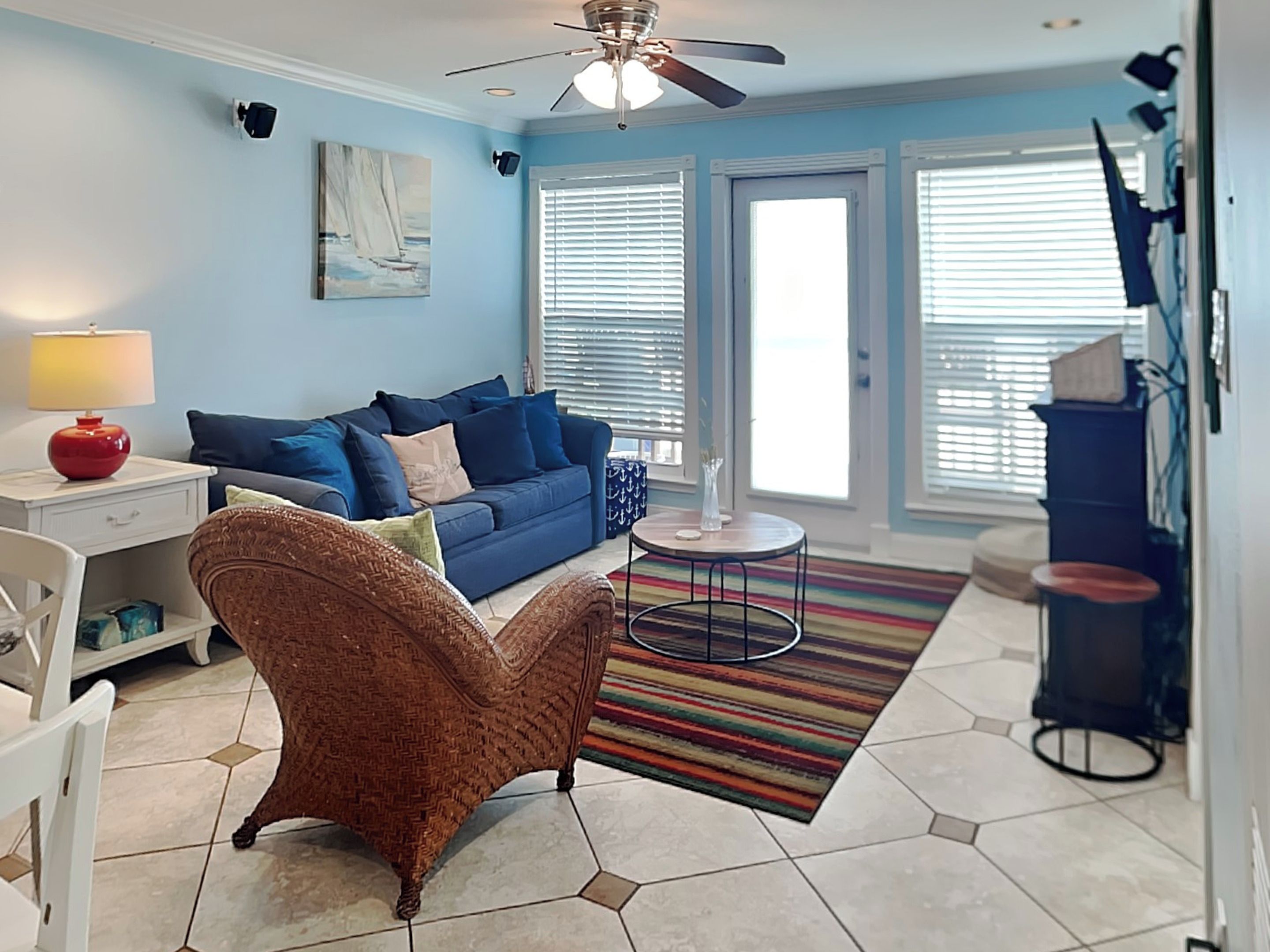 A living room with a blue sofa, a wicker chair, a small table, and a colorful rug.