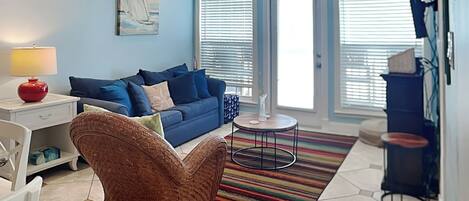A living room with a blue sofa, a wicker chair, a small table, and a colorful rug.