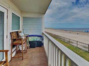 Un balcon avec vue sur la plage, des chaises en bois et une piscine gonflable bleue.