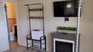 A bedroom with a four-poster bed, a TV mounted on the wall, a fireplace, and a small table with a chair.