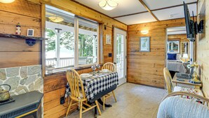 L’intérieur chaleureux d’un chalet avec un mur en pierre, des murs en bois, une table à manger avec des chaises, un lit et un téléviseur fixé au mur.