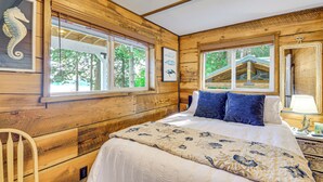 Une chambre à coucher dans une cabane en bois, avec un lit, deux fenêtres et un tableau représentant un hippocampe.