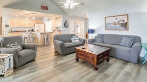 A spacious living area with a grey sofa, a wooden coffee table, and a grey armchair. A kitchen is visible in the background with wooden cabinets and a white refrigerator. - Bring Your Boat! Lakefront Home w/ Dock in Grove (Grove)