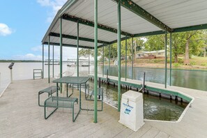Une zone abritée avec une table et des bancs, une pompe à eau, et une vue sur le lac et les bateaux.