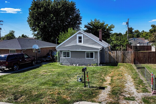 A residential house with a front yard, a basketball hoop, a driveway, and a wooden fence.